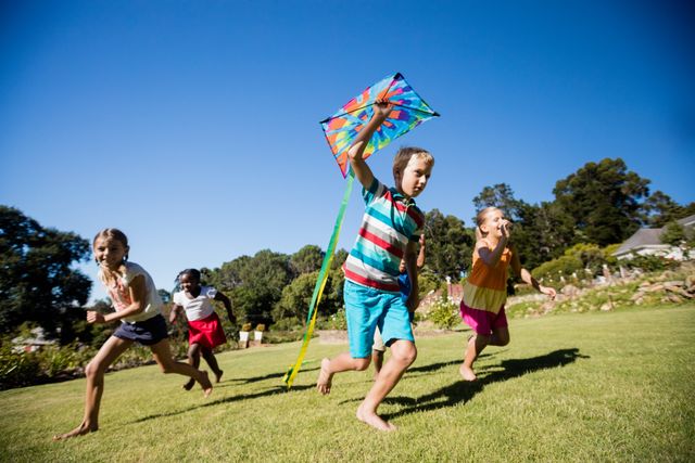 Children are running and playing with a colorful kite in a sunny park. The scene captures the joy and carefree nature of childhood, making it perfect for use in advertisements, educational materials, and family-oriented content. The bright colors and clear blue sky emphasize a cheerful and vibrant atmosphere.