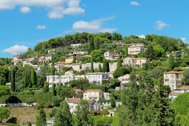 This picturesque hilltop village, with its lush greenery and clear blue sky, is ideal for travel blogs, nature magazines, and tourism brochures. It showcases beautiful residential architecture surrounded by nature, offering a serene countryside atmosphere perfect for promoting outdoor leisure activities and real estate in picturesque locations.
