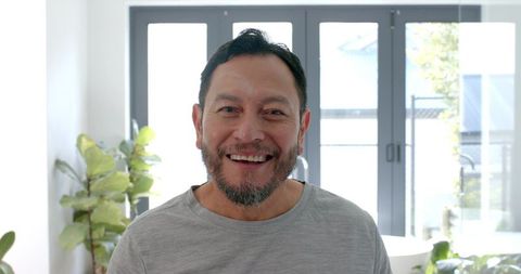 Senior Man Smiling Indoors with Greenery by Glass Doors