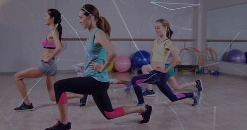 Women performing front lunges in studio group fitness class wearing colorful activewear