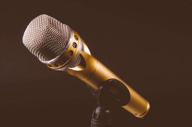Golden microphone mounted on black stand under studio lighting, useful for promoting music, podcasts, broadcasting, and audio recording services. Ideal for advertisements, blogs, or articles on sound production, music industry, and media.