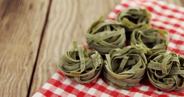 This visually appealing close-up image features six green fettuccine nests arranged on a rustic wooden table with a red and white checkered cloth. Ideal for use in food blogs, Italian cuisine websites, healthy eating articles, restaurant menus, or cooking classes advertisements.