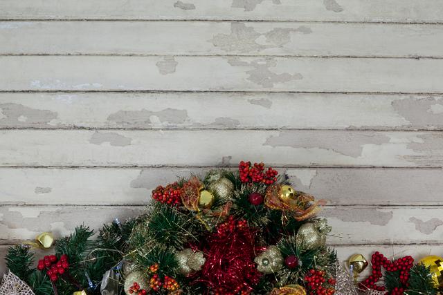 Christmas wreath adorned with red and gold ornaments, pine branches, and berries against a rustic wooden background. Ideal for holiday greeting cards, festive advertisements, seasonal blog posts, and social media content.