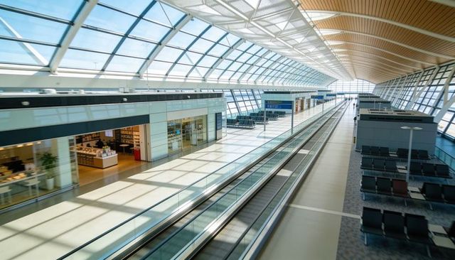 Sunlit airport concourse featuring dual moving walkways, glass atrium, retail and seating