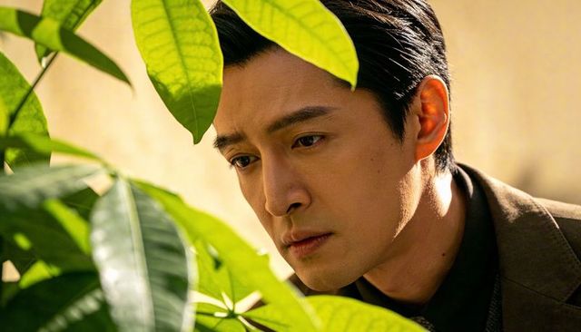 Introspective man peering through green leaves wearing brown suit warm sidelit indoor portrait