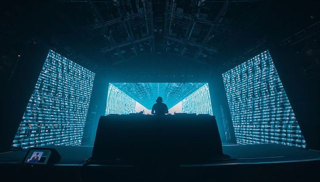 Silhouetted DJ Performing Behind Neon-Lit LED Walls on Club Stage with Futuristic Visuals