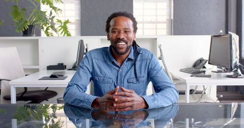 Confident entrepreneur smiling at work desk in modern office space