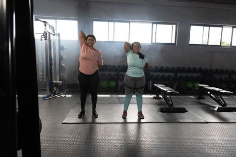 African american women stretching triceps together in sunlit gym for inclusive fitness