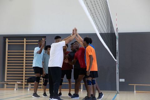 High-fiving diverse teenage male volleyball team celebrating win in indoor gymnasium huddle