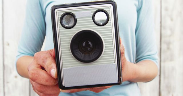 Person holding a vintage box camera closely, emphasizing its classic design. Ideal for websites and blogs about photography history, retro technology, and analog camera enthusiasts. Great for illustrating articles on vintage gadgets or as a nostalgic decor piece in a creative project.