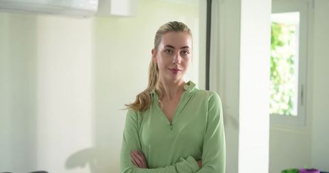 Confident blonde woman standing with crossed arms in bright minimalist interior