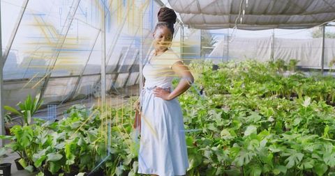 Confident woman posing in greenhouse nursery with potted plants and crossbody bag