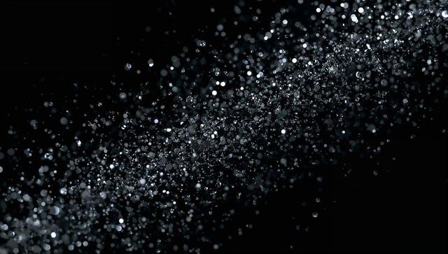 Glittering water spray forming diagonal stream with bokeh highlights on black background