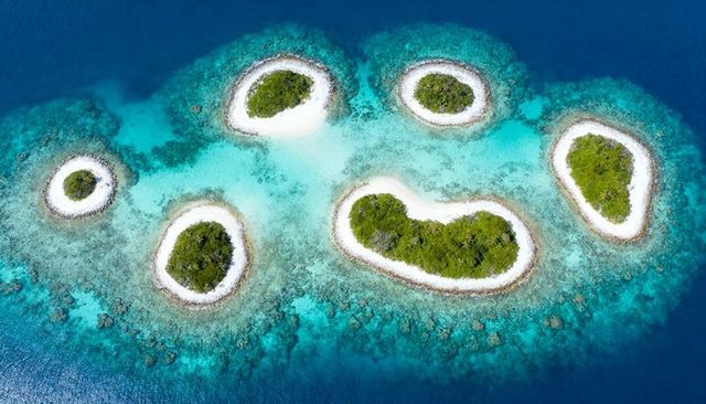 Aerial drone view showing seven tropical motu circling turquoise lagoon with sand rims