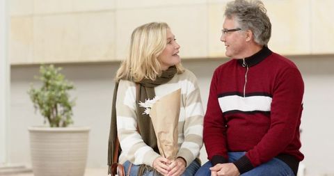 Mature couple sharing warm conversation on bench holding bouquet in bright indoor atrium