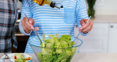 Middle-aged Woman Preparing Fresh Salad with Olive Oil