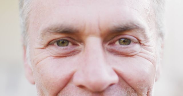 This close-up portrait of a senior man with green eyes smiling can be used in articles or advertisements focusing on aging, health, positivity among elders, or lifestyle content. It captures the natural expressions and features of aged individuals, making it ideal for topics related to life experiences, mental well-being, or healthcare for seniors.