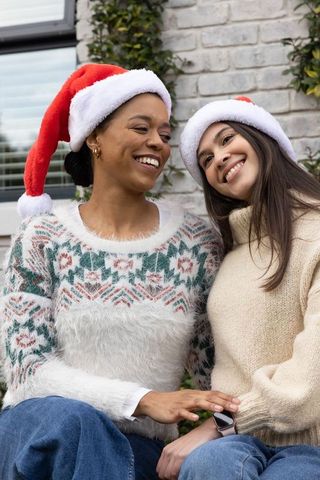 Smiling diverse friends wearing santa hats on porch in cozy knit sweaters celebrating holidays