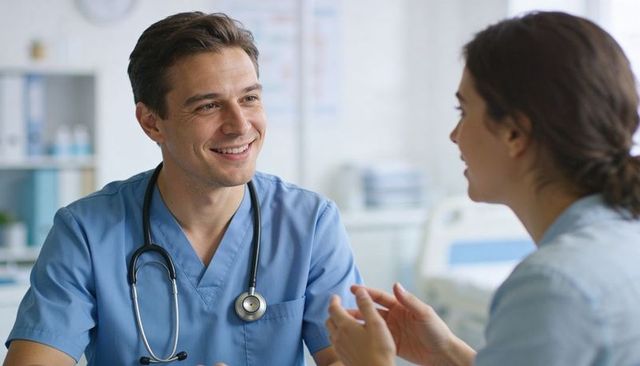 Smiling male clinician listening to colleague during compassionate patient consultation