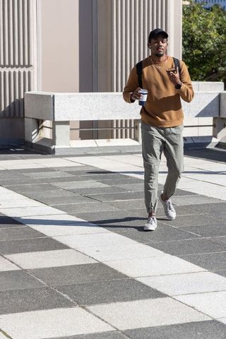 African American man walking across terrace carrying coffee and phone, casual commute