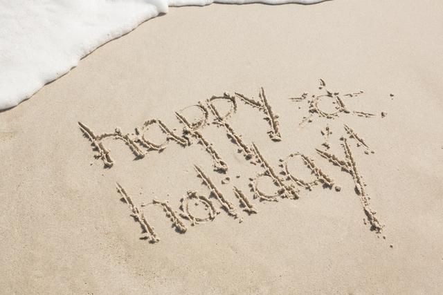 Happy holiday written on sand at beach