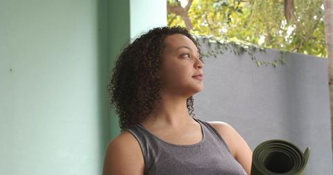 Sunlit african american woman holding yoga mat gazing outdoors preparing for morning yoga
