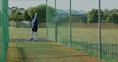 Indian cricket player practicing batting in outdoor net with protective gear and copy space