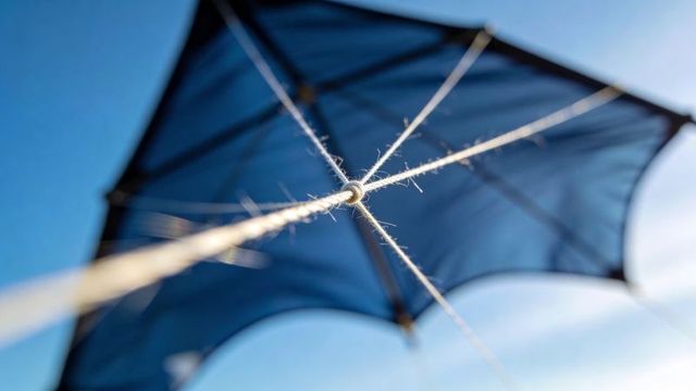 Closeup showing taut kite bridle knot and frayed fibers against bright blue sky