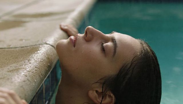 Serene portrait of woman resting at pool edge, eyes closed, water droplets on skin