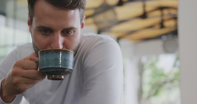 Man holding cup of hot beverage, enjoying peaceful moment. Great for lifestyle blogs, relaxing scenes, or advertisements focusing on coffee or tea brands.