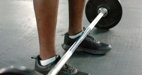Feet bracing for barbell deadlift african american male wearing black sneakers on gym mat