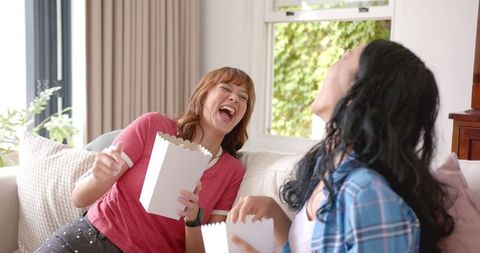 Young Women Laughing with Popcorn at Movie Day Inside