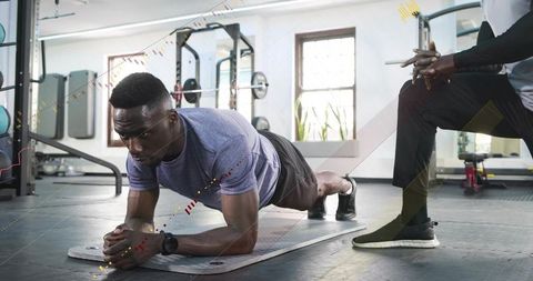 Man holding forearm plank while personal trainer coaching core workout in gym session