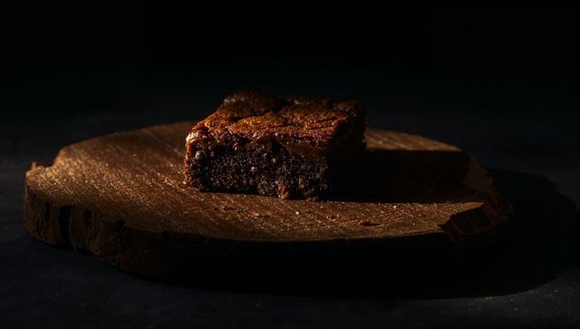 Spotlighting fudgy chocolate brownie on rustic wood slab with warm low-key lighting