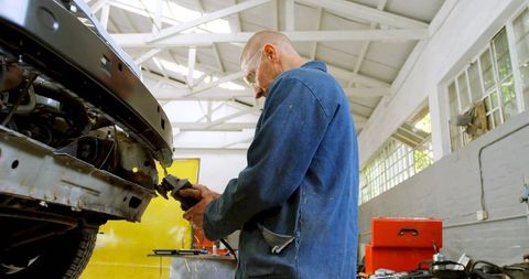 Grinding car frame with angle grinder in sunlit auto repair garage, mechanic at work