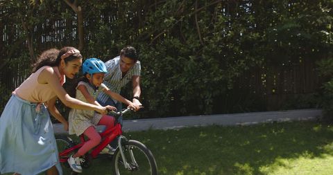 Family Bonding While Teaching Child to Ride Bike in Sunny Backyard