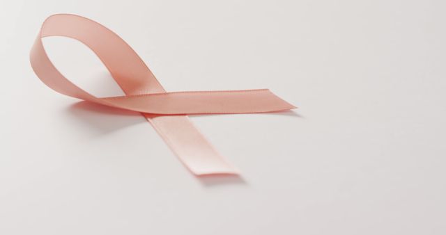 Pink ribbon lying on white background, representing breast cancer awareness and support. Ideal for health campaigns, support group materials, charity event promotions, and awareness month initiatives.