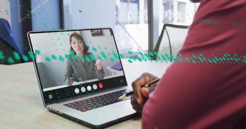 Remote meeting collaboration: man writing notes during video call with female presenter