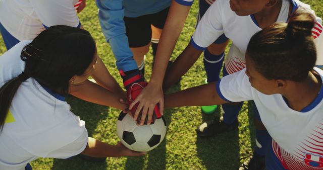 Team of young soccer players from diverse backgrounds uniting hands with a soccer ball, symbolizing teamwork and unity before a game. Ideal for use in articles, websites, or advertisements related to youth sports, teamwork, and diversity in sports.