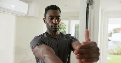 African american man performing resistance band shoulder stretch in bright home gym