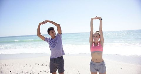 Young Couple Stretching on Sunny Beach in Athletic Attire