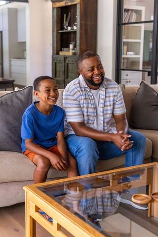 African american father and son smiling on sofa in contemporary open-plan living room