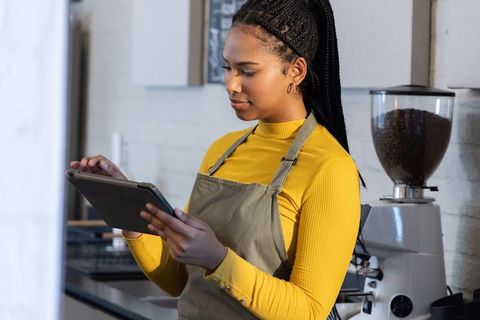 African American Barista Using Tablet in Modern Cafe with Espresso Grinder and Chalkboard