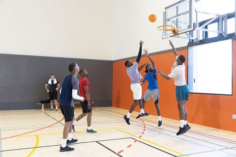 Diverse male teammates playing pickup basketball indoors jumping and reaching for hoop
