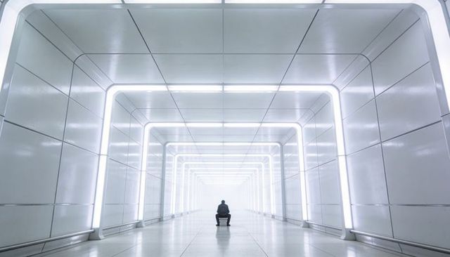 Solitary Man Sitting in Futuristic Illuminated Tunnel with Symmetrical Neon Arches