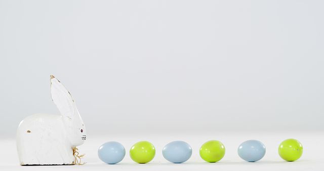 A white ceramic Easter bunny is positioned next to a row of pastel-colored eggs, with copy space - Download Free Stock Photos Pikwizard.com