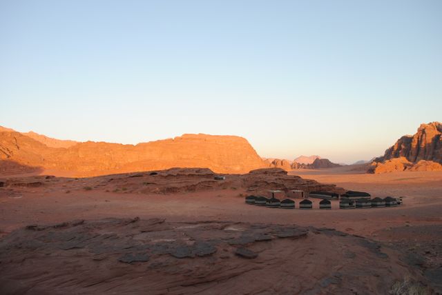 Traditional tents are seen amidst desert landscape bathed in warm sunset light. Ideal for travel content, adventure tourism, nature exploration, and storytelling. The isolated campsite in the vast desert evokes feelings of serenity, solitude, and the beauty of untouched nature.
