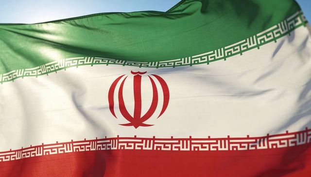 Waving iran flag close-up showing red emblem and kufic border backlit fabric detail