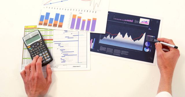 Hands holding calculator and pen analyzing financial charts and graphs. Useful for illustrating topics about business analysis, financial reports, data analysis, and market research. Perfect for use in business presentations, financial websites, and economics education.