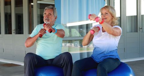 Senior Couple Exercising with Dumbbells on Fitness Balls